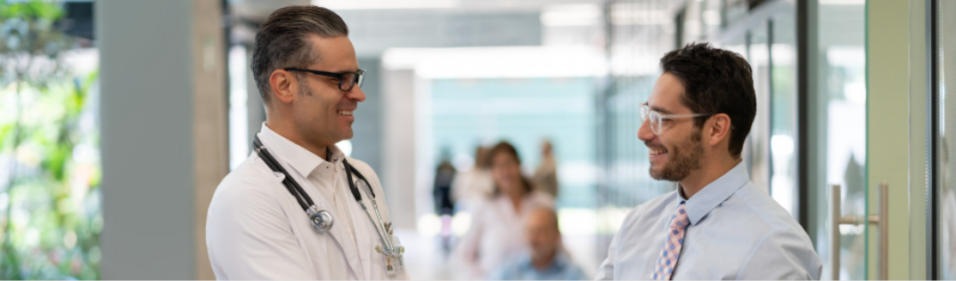 Two men shaking hands in a white coat and glasses smiling at each other