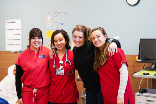 nurse student smiling at the camera together in front of hospital bed