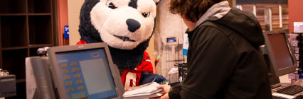 Wolfie mascot talking to clerk at computer